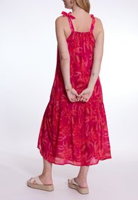 Helles pinkes Kleid mit floralem Muster, verstellbaren Bindeträgern und schichtigem Stoff für eine fließende Passform. Getragen mit beigen Espadrilles.