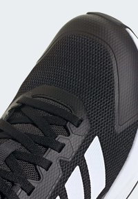Chaussure de sport noire avec une tige en mesh texturé et des superpositions synthétiques, des lacets noirs et trois rayures blanches sur le côté.