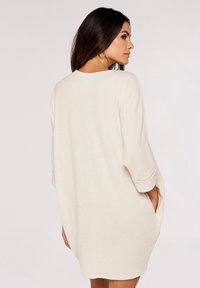 Ljusbeige, ribbad stickad klänning med avslappnad passform, trekvartslånga ärmar och sidofickor, med rund halsringning och mjukt material.
