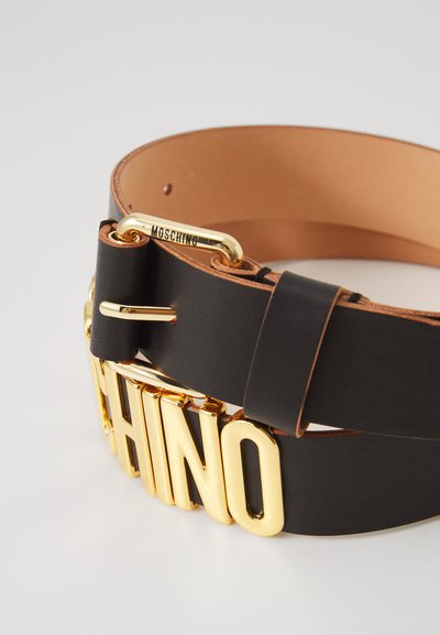Mustade nahast vöö, millel on silmapaistev kuldne "MOSCHINO" logo pandla, sujuva tekstuuriga ja kontrastse beeži siseküljega.