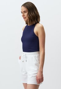 Canotta a coste blu navy con design senza maniche, abbinata a pantaloni corti bianchi con cintura elastica e cordino. Texture liscia, vestibilità su misura.