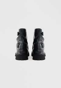 Mustad nahast pahkluu saapad, millel on lõdva kujundusega kaks reguleeritavat rihma ja jäme kummist tald. Sile viimistlus, mustriteta.