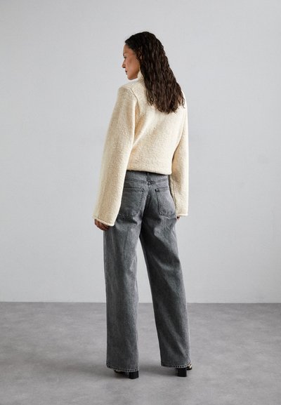 Light beige textured, long-sleeve sweater with a high neck, paired with loose-fitting gray jeans. The outfit has no visible patterns or accents.