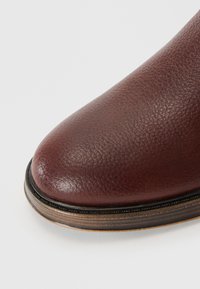 Botte en cuir bordeaux avec une finition texturée, un bout rond et une bordure marron contrastante le long de la semelle.