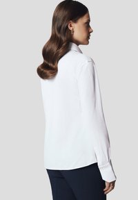 Biała koszula z długim rękawem, klasycznym kołnierzykiem i zapięciem na guziki, z gładką fakturą i luźnym krojem.