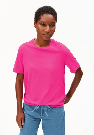 Fuchsia katoenen T-shirt met een ronde hals, korte mouwen en een losse pasvorm. Draagt lichtblauwe broek met trekkoord.