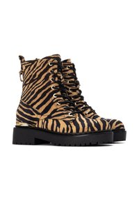 Botas de ante a rayas de cebra en tonos marrón y negro, con ojetes metálicos, cordones negros y una suela gruesa de goma negra con un acento dorado.