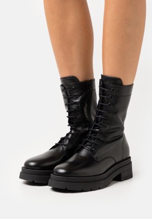 Black leather ankle boots with a rounded toe, lace-up front, and rugged rubber sole. Features a slightly glossy finish and padded collar.