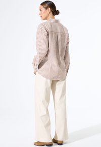 Gestreepte blouse in beige en crème, gecombineerd met crème wijde broek. Heeft lange mouwen en een rugplooi-detail, gladde stofstructuur.