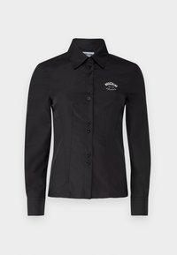 Maglietta nera con un design aderente, maniche lunghe e colletto a punta. Presenta una chiusura con bottoni e un logo ricamato sul petto.