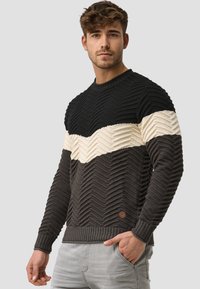 Sweter w czarno-kremowy wzór w zygzaki, z teksturowanym splotem; ściągacze u dołu i na mankietach; posiada małą brązową naszywkę z logo z boku.