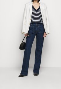 Blazer blanc, pull col en V rayé marine, jean évasé en denim foncé, sac à main noir et chaussures noires à bout pointu. Lignes épurées et coupe moderne.