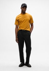 Sininen lyhythihainen t-paita, mustat housut ja mustat kengät. Yksinkertainen muotoilu, pehmeä rakenne, hyvin istuva ja yksinkertainen lippalippis.