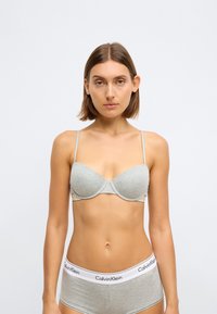 Sutiã acolchoado cinza com alças ajustáveis, design sem costuras, e logótipo da Calvin Klein exibido na faixa elástica da roupa interior a condizer.