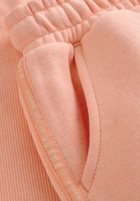 Tröjfabric i persikofärg med ribbat mönster, elastisk midja och sidoficka med vit branding på kanten.