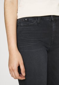 Jeans de denim oscuro con un ajuste slim, que presentan un logo de Calvin Klein en el bolsillo frontal, cierre de botón y detalles de costura mínimos.