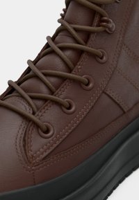 Gros plan d'une botte en cuir marron avec des lacets ronds marron passant par six œillets métalliques et une semelle épaisse noire.