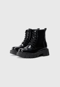 Black patent leather ankle boots with a chunky black rubber sole, round toe, thick laces, and pull tab at the back.