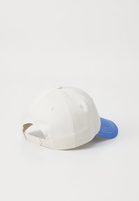 White baseball cap with a blue brim, made of cotton. Adjustable strap at the back, textured surface with visible stitching details.