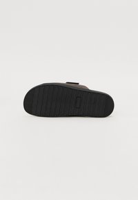 Flat-soled sandal featuring a black rubber outsole with ridges, a brown suede upper, and a hook-and-loop strap for secure fitting.