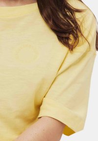 Geel T-shirt met korte mouwen en een relaxte pasvorm. Bevat een subtiele, verhoogde logo op de borst en opgerolde mouwmanchetten. Zachte textuur.