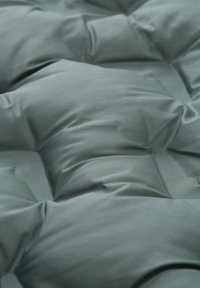 Pikowany materiał w stonowanym odcieniu teal, charakteryzujący się gładką fakturą, widocznymi szwami oraz uniesionymi sekcjami, co daje efekt wyściółki.