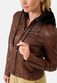 Braune Lederjacke mit schwarzer Kapuze, ausgestattet mit Reißverschlusstaschen und Zugbändern. Abgestoßene Textur und taillierte Passform mit Akzentnähten.