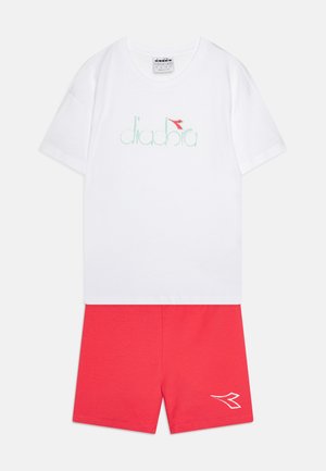 Bijela pamučna majica s mentolno zelenim "diadora" logotipom i crvenom oznakom; uparen s crvenim pamučnim šorcima koji imaju bijeli detalj logotipa.