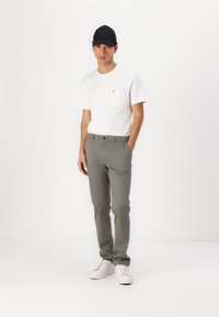 Weißes T-Shirt mit einer Tasche, graue Hose und weiße Turnschuhe. Die Person trägt eine schwarze Mütze. Minimalistisches Design vor einem schlichten Hintergrund.
