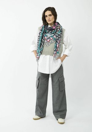 Gilet en laine gris sur une chemise blanche, associé à un pantalon cargo large gris. Une écharpe à motifs intègre des couleurs comme le rose et le turquoise.