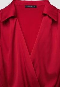 Blusa rossa con ampio colletto e scollatura a V profonda, con etichetta del marchio "Calliope" in taglia piccola.