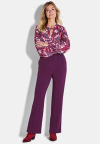 Kleurrijke, gebloemde blouse met een sleufhals, gecombineerd met hoog-getailleerde paarse broek en rode suède enkelboots.