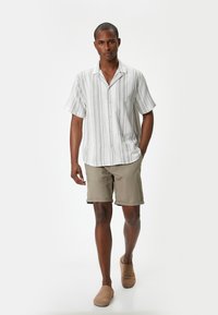 Camisa de manga corta, con botones, a rayas horizontales en blanco y gris, combinada con pantalones cortos beige y zapatos de lona color marrón claro.