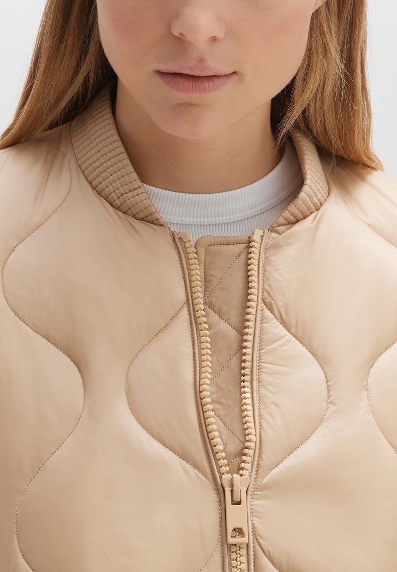 Quilted beige Lederbomberjacke mit geripptem Kragen, zentralem Reißverschluss und strukturierten Akzenten an den Schultern und Ärmeln.