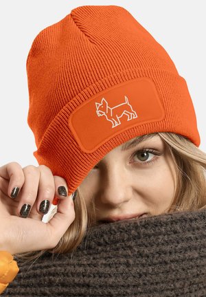 Orange knitted beanie featuring a white dog graphic on a patch. Textured fabric with a snug fit, worn slightly tilted over the forehead.
