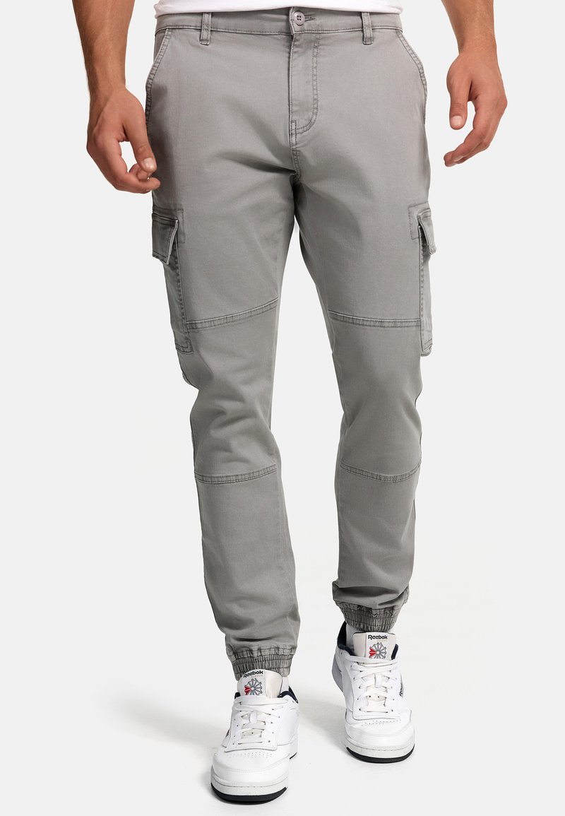 Helle graue Cargo-Hosen mit elastischen Bündchen, mehreren Seitentaschen und Steppdetails, kombiniert mit weißen Sneakern.