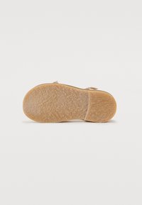 Semelle en caoutchouc marron avec une surface texturée et un léger profilé. Présente un bandeau étroit pour le soutien avec un dessus de couleur claire.