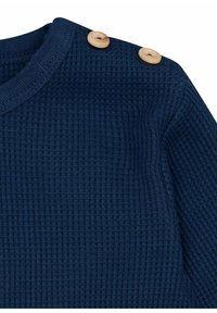 Marineblaues ribbeldickes Strickoberteil mit einem strukturierten Stoff, das an der linken Schulter mit Holzknöpfen versehen ist, um zusätzliche Details zu bieten.