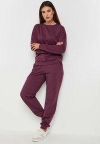 Sudadera morada y joggers a juego hechos de una tela suave. La sudadera tiene un cuello redondo; los joggers cuentan con puños y cinturilla elásticos.