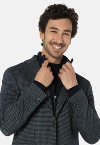 Marineblauwe houndstooth-gepatroneerde blazer met een grijze binnenkant, voorzien van een ritssluiting bij de kraag, knopenmanchetten en een getailleerde pasvorm. De textuur lijkt gestructureerd.