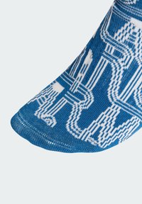 Kék kötött zokni fehér absztrakt mintával, sima textúrával és lekerekített orral. Az anyag légáteresztőnek és rugalmasnak tűnik.