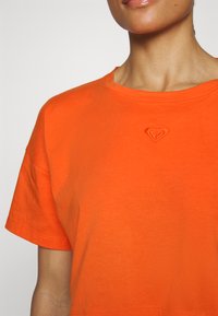 Short-sleeve T-shirt in bright orange cotton. Features a round neckline and an embroidered heart logo on the chest. Smooth texture.