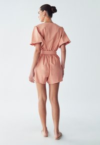 Persikavärvi kombineeritud rõivad lühikeste varrukatega ja kergelt vööga. Kerge kangas, hästi istuv lõige ja lühike disain.