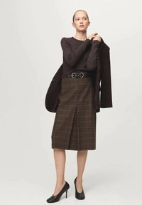 Hnedý dlhý rukáv s tričkom skombinovaným s károvanou ceruzkovou sukňou s predným záhybom. Oblečené s čiernym opaskom a čiernymi vysokými podpätkami.