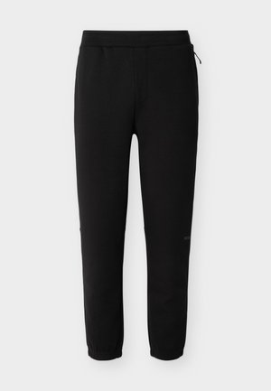 Pantalon de jogging noir avec taille élastique et poignets aux chevilles, équipé d'une petite fermeture éclair latérale et d'un logo discret de la marque sur la jambe droite.