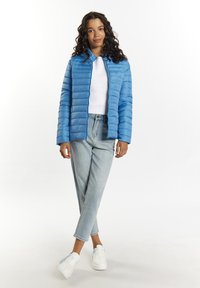 Lyseblå pufferjakke med vandret syninger, båret over en hvid sweater. Kombineret med lyseblå jeans og hvide sneakers.