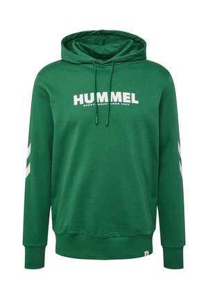 Personne portant un sweat à capuche hummel vert et un pantalon vert assorti avec le logo blanc hummel sur la poitrine, les manches et la cuisse.