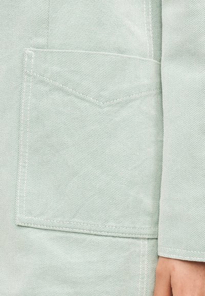 Τσέπη από ανοιχτό μπλε τζιν με ορατή διαγώνια ραφή και μέρος του χεριού ενός ατόμου στο κάτω δεξιό άκρο.