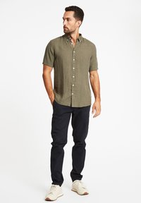 Olijfgroene linnen shirt met korte mouwen, knoopsluitingen aan de voorkant, gecombineerd met zwarte broek en lichtgekleurde sneakers. Eenvoudig ontwerp, casual pasvorm.