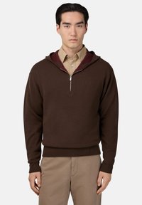 Hnedá mikina na zips s burgunďskou podšívkou kapucne, pletená textúra, rebrované manžety a lem. Nosená cez svetlohnedú košeľu s golierom.